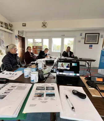 A classroom at North Oxford Marine Training with students sat at desks in a horseshoe shape with lots of course material and equipment listening to the instructor