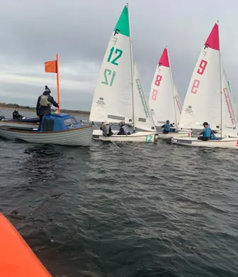 A group of dinghies and a race boat preparing to start a race on the reservoir at the Royal Hospital School Sailing Academy, Ipswich