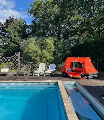 Outdoor swimming pool with a bright orange liferaft alongside that is used during the basic sea survival course