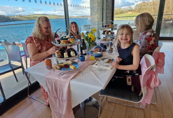 Two adults and two children enjoying afternoon tea at the on-site cafe at Llandegfedd Watersports, Pontypool, Gwent