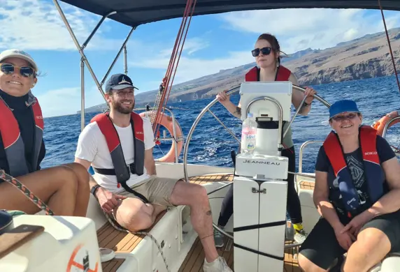 Four people sailing on a yacht on a sunny day with one person helming (steering) and the others relaxing