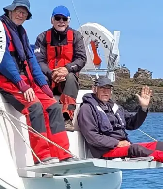 Three men sitting off the back of yacht - one of them is waving