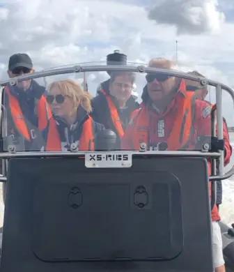 Five people wearing life jackets standing behind the console of a large rigid inflatable boat (RIB) on the water on a cloudy day