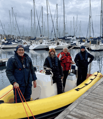 Four people preparing to pull away from the jetty on a yellow rigid inflatable boat (RIB) with lots of masted yachts in the background