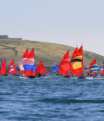 A fleet of Mirror dinghies with bright red sails racing on the water during Abersoch Mirror Week at South Caernarvonshire Yacht Club, Abersoch, Wales