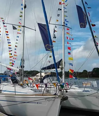 Yachts with lines of coloured flags running up either side of the masts moored alongside a jetty