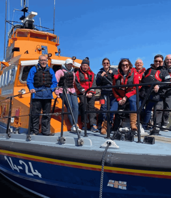 A group of volunteers standing on the front deck of an RNLI rescue boat on a sunny day