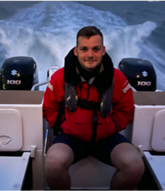 A young man in a red coat wearing a life jacket sitting at the back of power boat with two engines speeding over the water