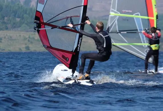 Two windsurfers skimming across the water with the shore in the distance